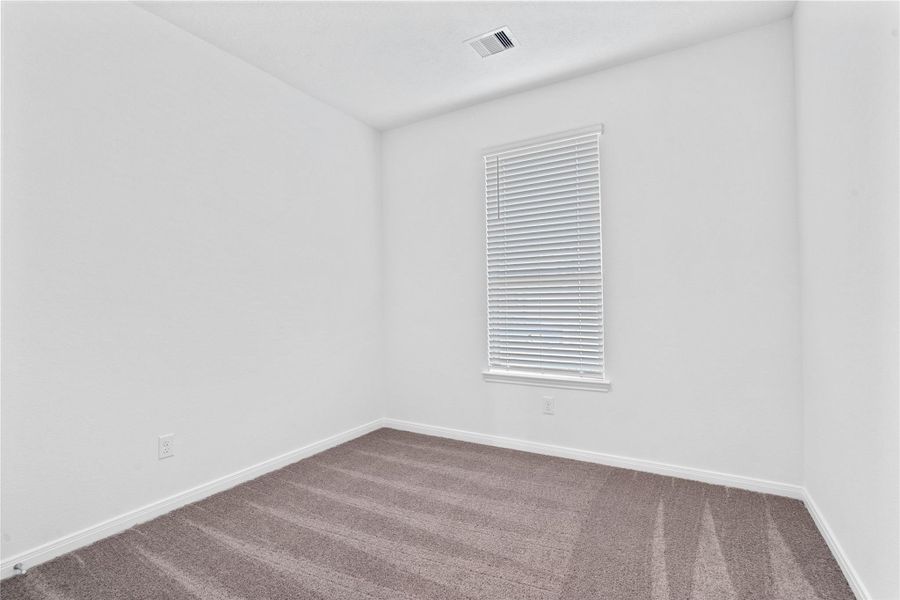 This secondary bedroom combines comfort and style, featuring plush carpeting, neutral paint, a large window with blinds, and a spacious closet.