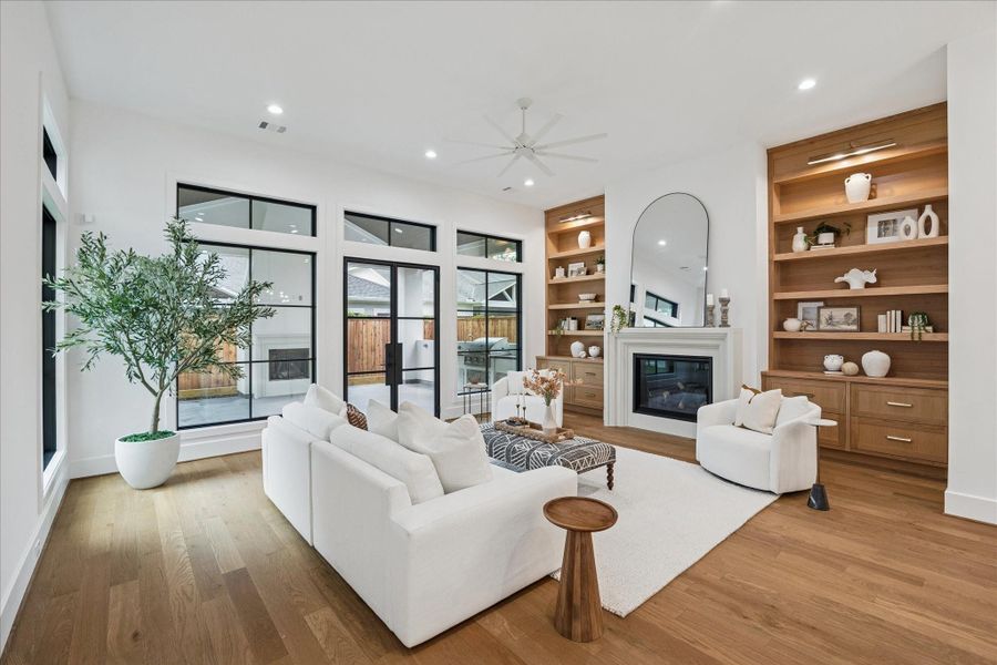 Floor-to-ceiling windows frame views of the covered patio and outdoor fireplace. Custom oak built-ins flank a sleek gas fireplace, adding balance and warmth. The open flow between kitchen, dining, and living creates a cohesive environment for daily living and entertaining. *Previous Project*