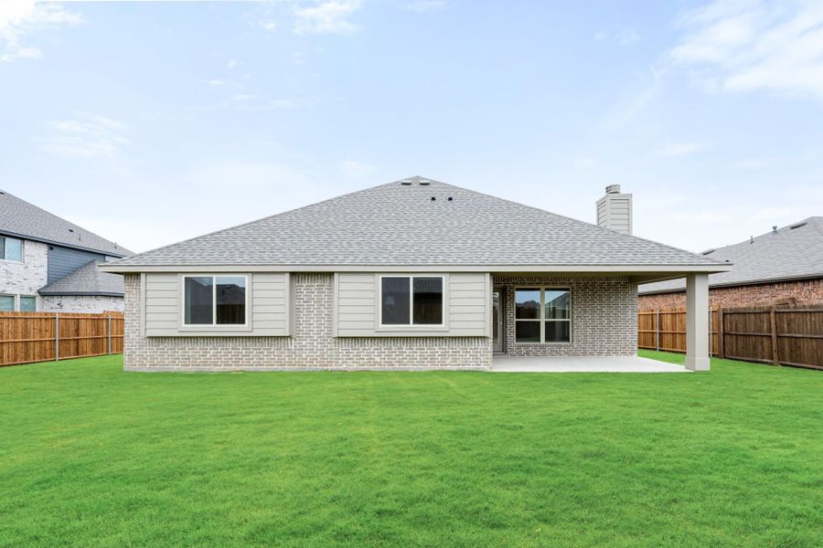Rear view of single-story brick home with covered patio, large green lawn, and wood privacy fence.