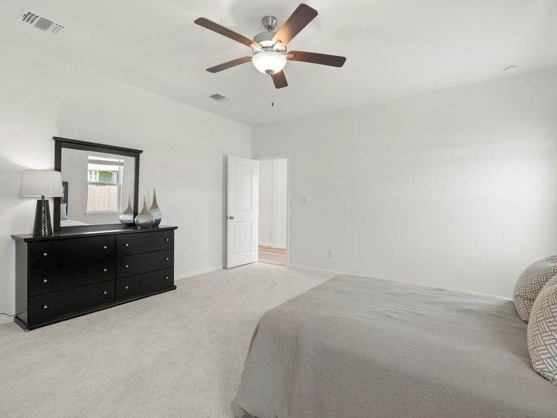 A well-lit bedroom features plush carpeting and a modern ceiling fan.