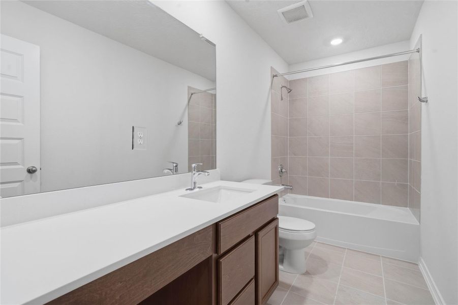 The secondary bathroom offers tile flooring, a bath/shower combination with a stylish tile surround, rich stained wood cabinetry, elegant light countertops, a mirror, and sleek fixtures with modern finishes. The secondary bathroom offers tile flooring, a bath/shower combination with a stylish tile surround, rich stained wood cabinetry, elegant light countertops, a mirror, and sleek fixtures with modern finishes.