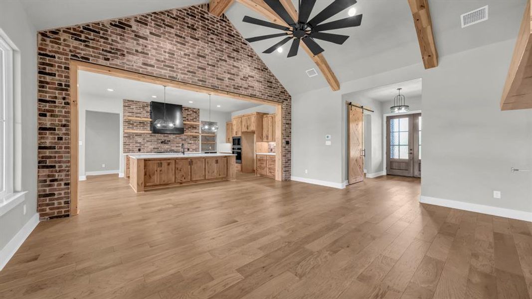 Spacious interior featuring wood-finish flooring, a vaulted ceiling with exposed wood beams, and a large ceiling fan