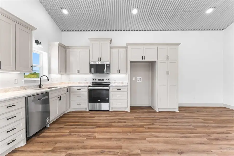 Kitchen featuring stainless steel appliances, light wood-type flooring, white cabinetry, light stone countertops, and recessed lighting Kitchen featuring stainless steel appliances, light wood-type flooring, white cabinetry, light stone countertops, and recessed lighting