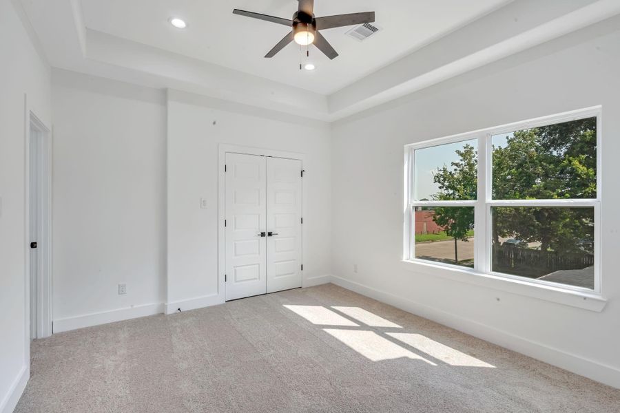 Spacious primary bedroom in the second floor featuring abundant natural light, tray ceilings, plush carpet flooring, and dual closets with access to the private ensuite bath.