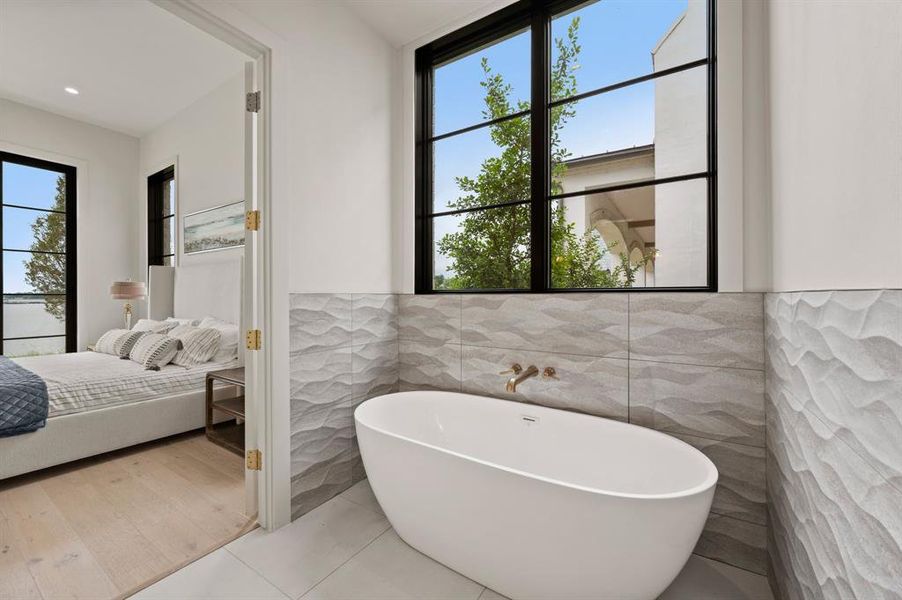 Ensuite bathroom featuring tile walls, a soaking tub, wainscoting, and tile patterned flooring Ensuite bathroom featuring tile walls, a soaking tub, wainscoting, and tile patterned flooring