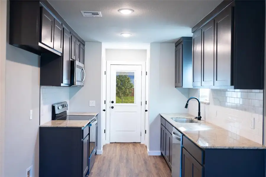 Kitchen with stainless steel appliances, a sink, wood finished floors, light stone counters, and tasteful backsplash