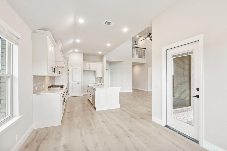 Open kitchen with white cabinets, center island, and light wood floors leading to living area