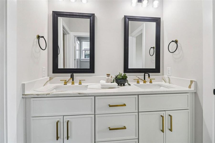 Dual vanity featuring white cabinetry with gold-tone hardware, undermount sinks, and a stone countertop