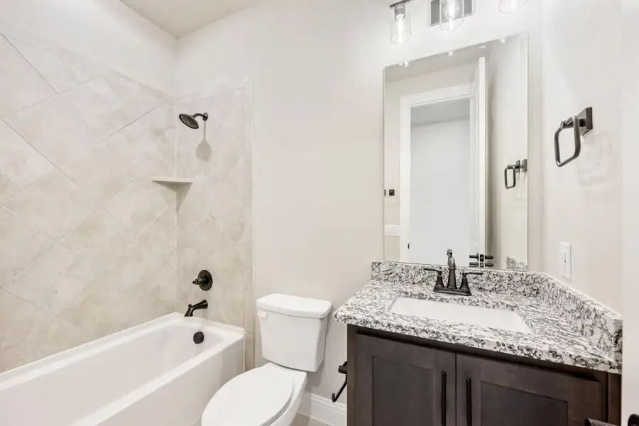 Bathroom with tiled tub-shower combo, dark wood vanity, granite countertop, and oil-rubbed bronze fixtures