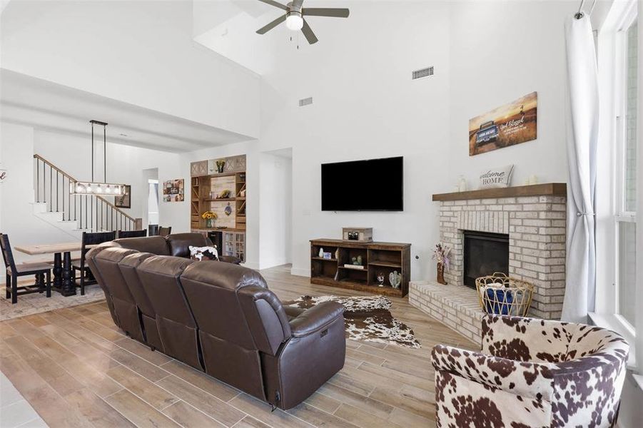 Spacious living room featuring high vaulted ceilings, light wood-finish flooring, and a whitewashed brick fireplace with a wood mantel