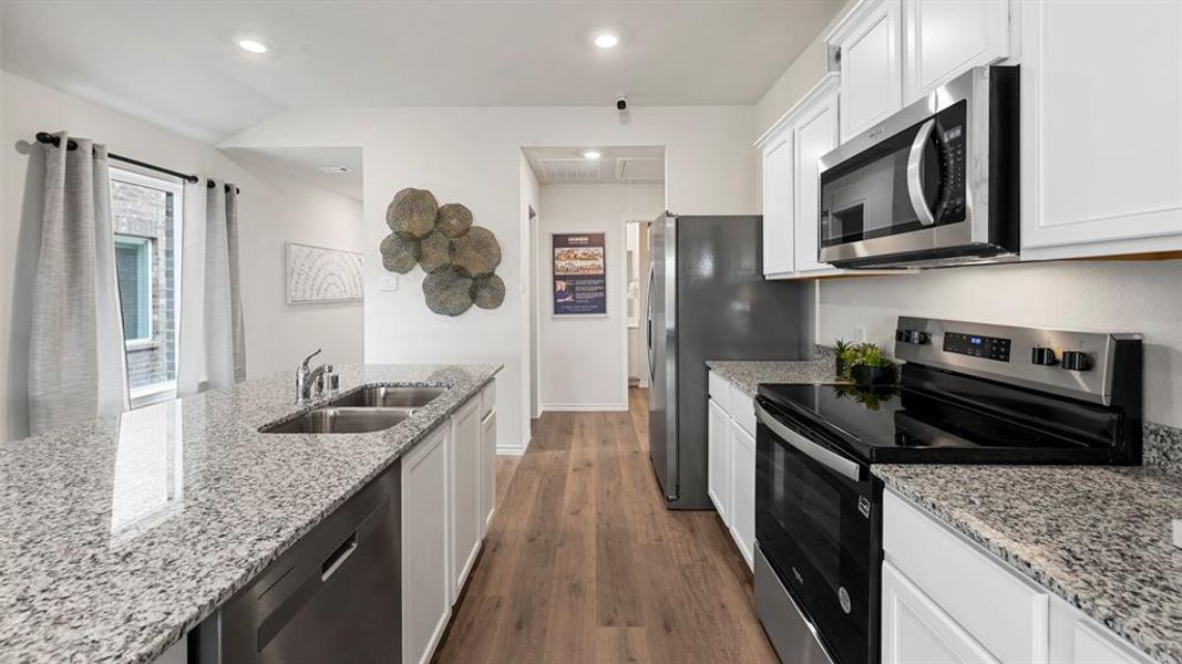 Kitchen featuring appliances with stainless steel finishes, white cabinetry, light stone counters, recessed lighting, and lofted ceiling Kitchen featuring appliances with stainless steel finishes, white cabinetry, light stone counters, recessed lighting, and lofted ceiling