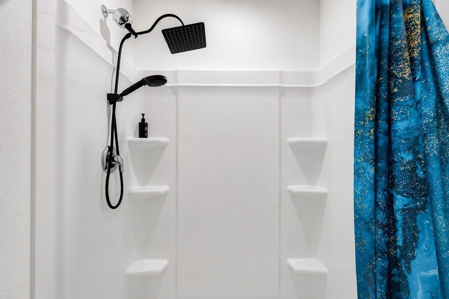 Oversized walk-in shower featuring a modern rainfall showerhead, handheld sprayer, and built-in corner shelving.