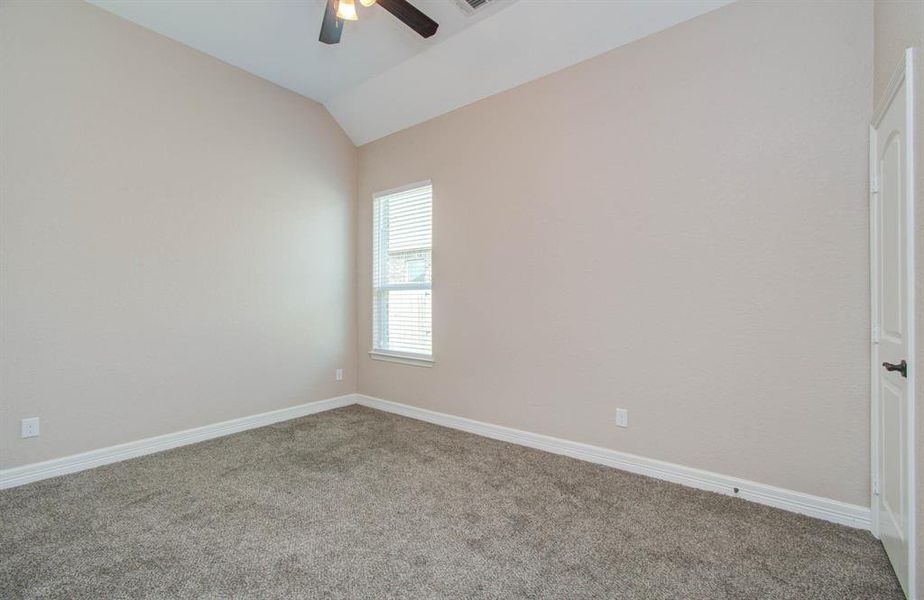 This is a bright, empty room with neutral-colored walls and carpeted flooring, featuring a ceiling fan and natural light from a window.