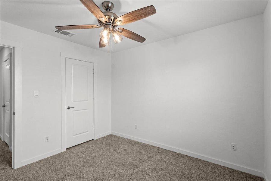A well-lit bedroom features plush carpeting and a modern ceiling fan.