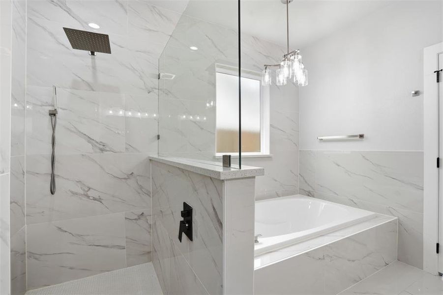 Contemporary bathroom featuring a spacious walk-in shower with a rainfall showerhead, a separate soaking tub, extensive marble-look tile work, a frosted window, and a modern chandelier