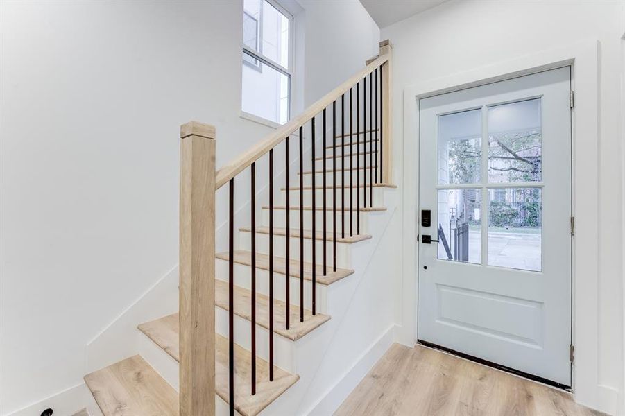 Entryway with beautiful window panes, luxury vinyl plank flooring and matching staircase and banister, with wrought iron railing.