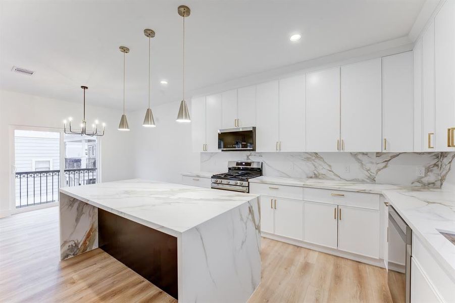 This stunning kitchen features gold hardware, quartz countertops, gas range, and stainless steel appliances. There is plenty of storage space in the cabinets.