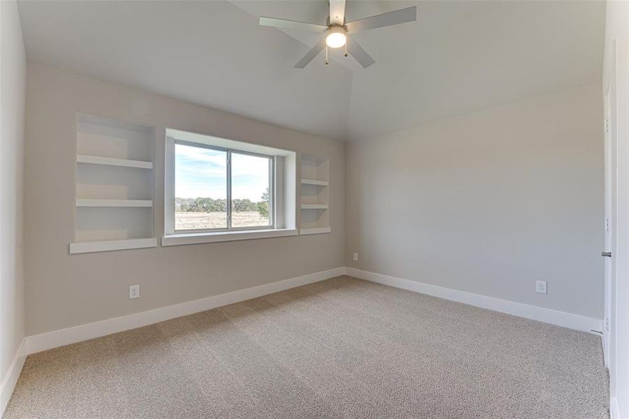 Carpeted empty room featuring built in shelves and ceiling fan