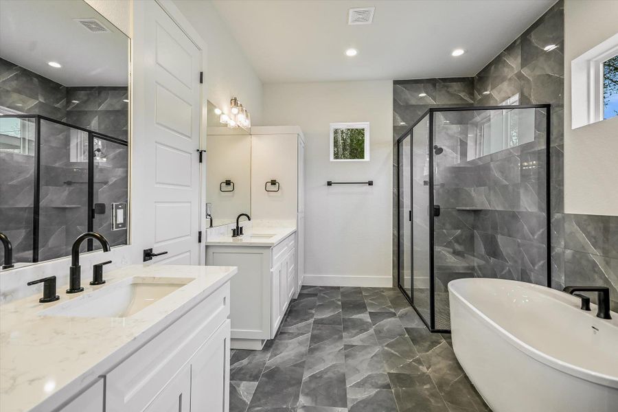 Bathroom featuring two vanities, a marble finish shower, a freestanding tub, plenty of natural light, and recessed lighting