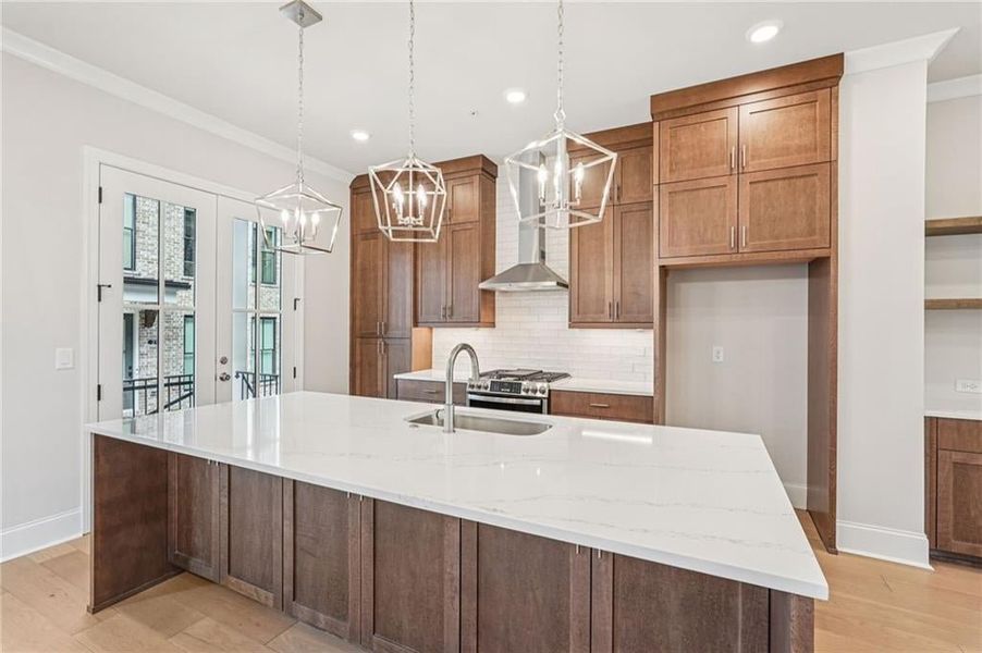 Kitchen featuring light stone counters, light wood finished floors, wood finish cabinets, pendant lighting, and crown molding