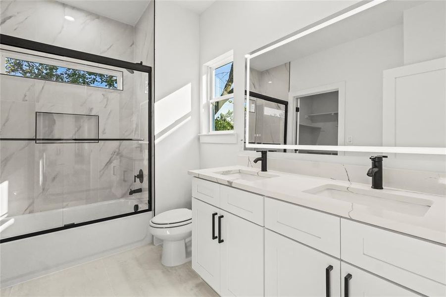 Full bathroom with combined bath / shower with glass door, double vanity, and light tile patterned floors Full bathroom with combined bath / shower with glass door, double vanity, and light tile patterned floors