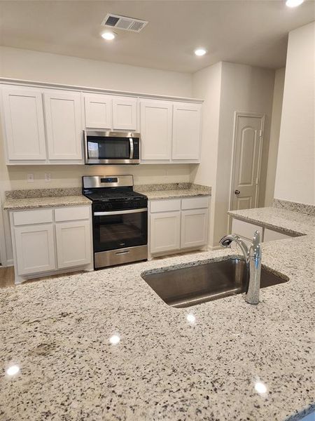 Kitchen with stainless steel stove, white cabinetry, recessed lighting, and light stone countertops Kitchen with stainless steel stove, white cabinetry, recessed lighting, and light stone countertops