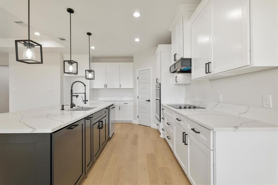 Kitchen featuring white cabinets, under cabinet range hood, pendant lighting, and an island with sink