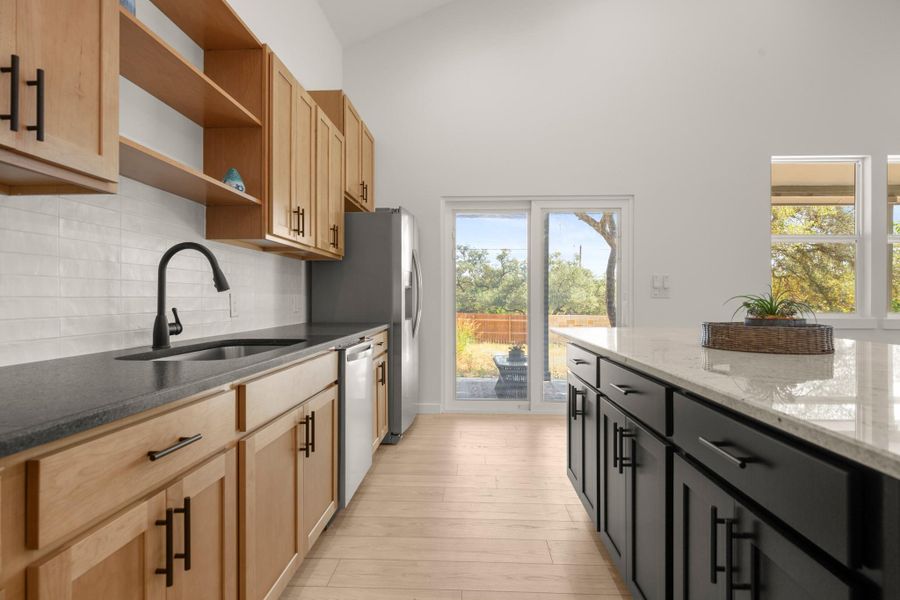 Kitchen featuring dark stone countertops, open shelves, decorative backsplash, light wood-type flooring, and dishwasher