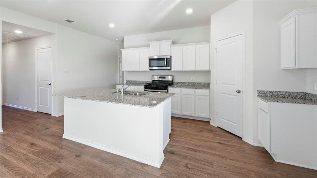 Kitchen with light stone countertops, white cabinetry, appliances with stainless steel finishes, a center island with sink, and recessed lighting Kitchen with light stone countertops, white cabinetry, appliances with stainless steel finishes, a center island with sink, and recessed lighting