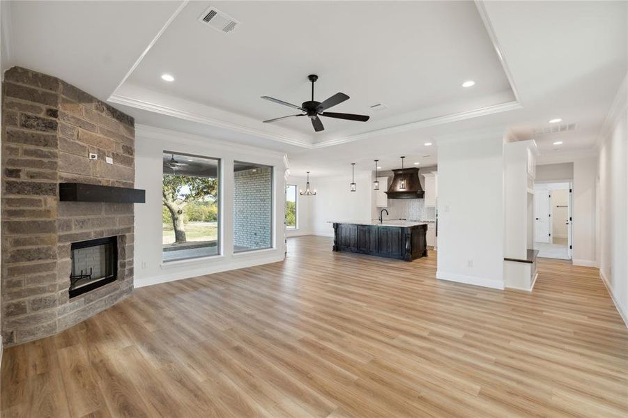 Unfurnished living room featuring ceiling fan, light hardwood / wood-style flooring, a tray ceiling, and a fireplace