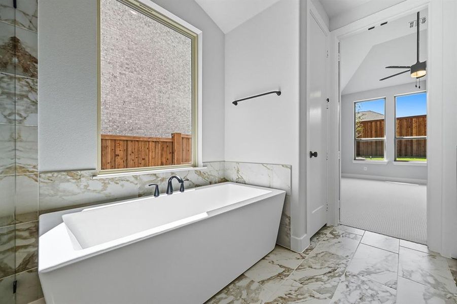 Full bathroom featuring light marble finish floors, a freestanding bath, tile walls, a ceiling fan, and a wainscoted wall