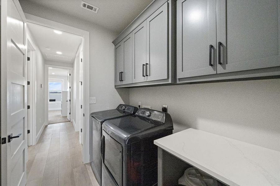 Laundry area featuring light wood-look tile floors, washer and dryer, cabinet and counter space for folding area.