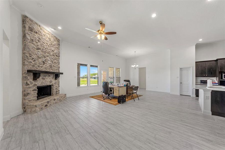 Living room with a stone fireplace, baseboards, a desk, a ceiling fan, and light wood-type flooring