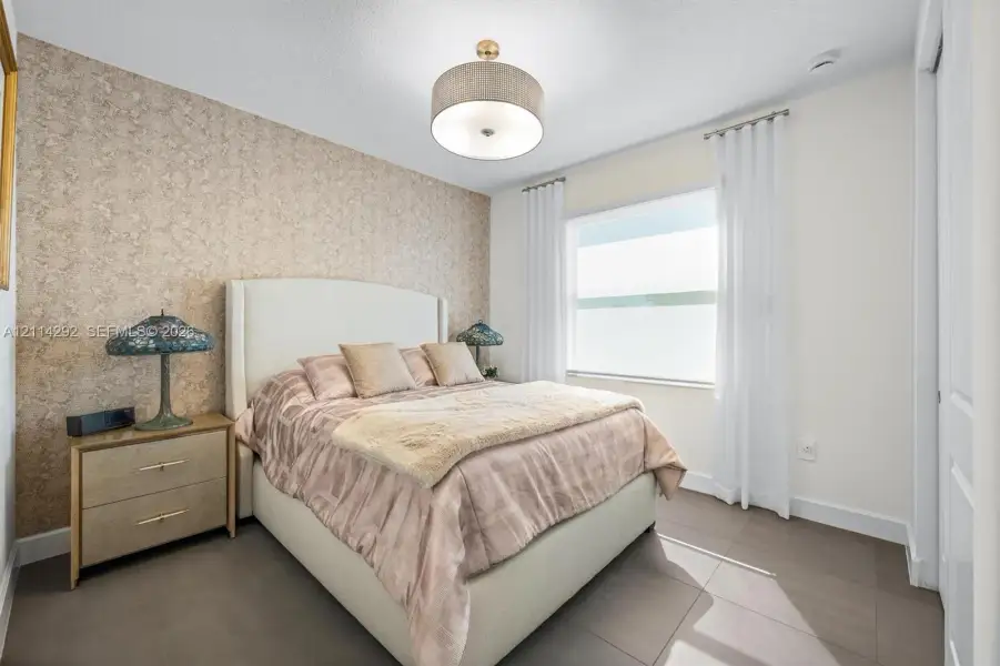 Textured accent wall, large window with neutral-toned treatments, drum-style ceiling light fixture, and ceramic tile flooring