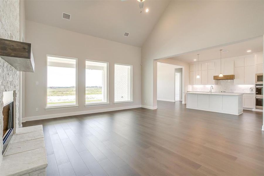 Unfurnished living room with a stone fireplace, sink, wood-type flooring, and high vaulted ceiling