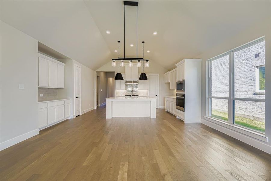 Kitchen featuring backsplash, vaulted ceiling, white cabinetry, pendant lighting, and light wood-style floors Kitchen featuring backsplash, vaulted ceiling, white cabinetry, pendant lighting, and light wood-style floors
