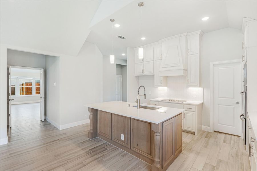 Kitchen with large wood island, white cabinets, pendant lights, and light wood-look tile floors