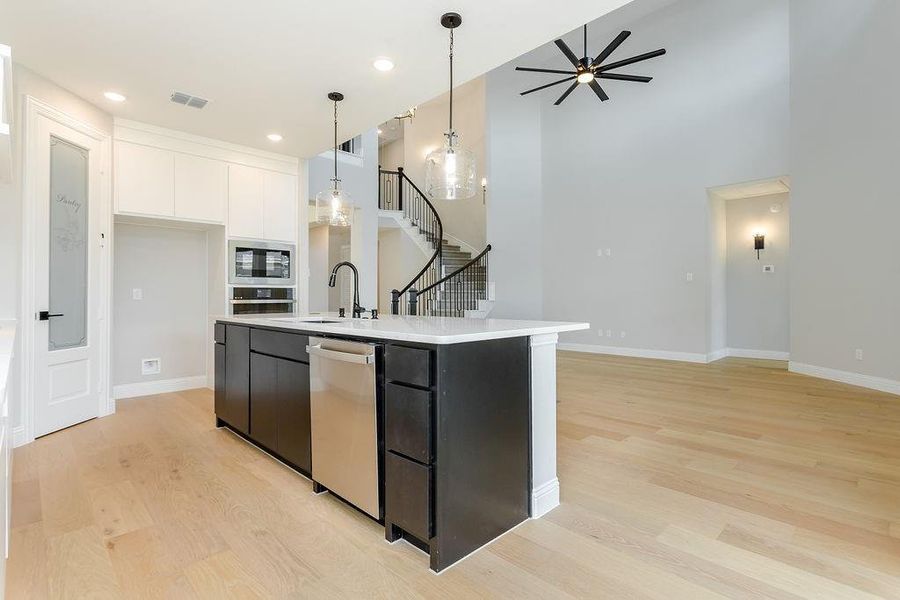 Kitchen with stainless steel dishwasher, white cabinetry, light wood-type flooring, and hanging light fixtures