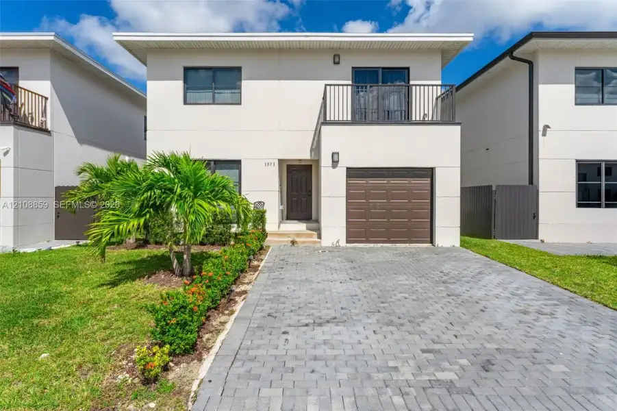 Two-story residence featuring a smooth stucco exterior, a paved stone driveway, an attached garage, and a second-story metal-railed balcony
