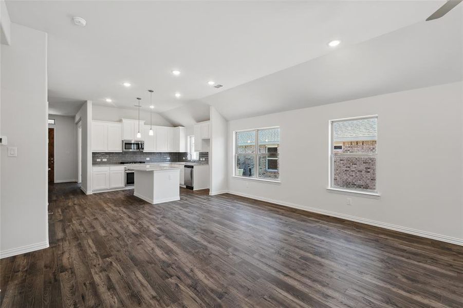 Kitchen with open floor plan, a center island, vaulted ceiling, stainless steel appliances, and backsplash