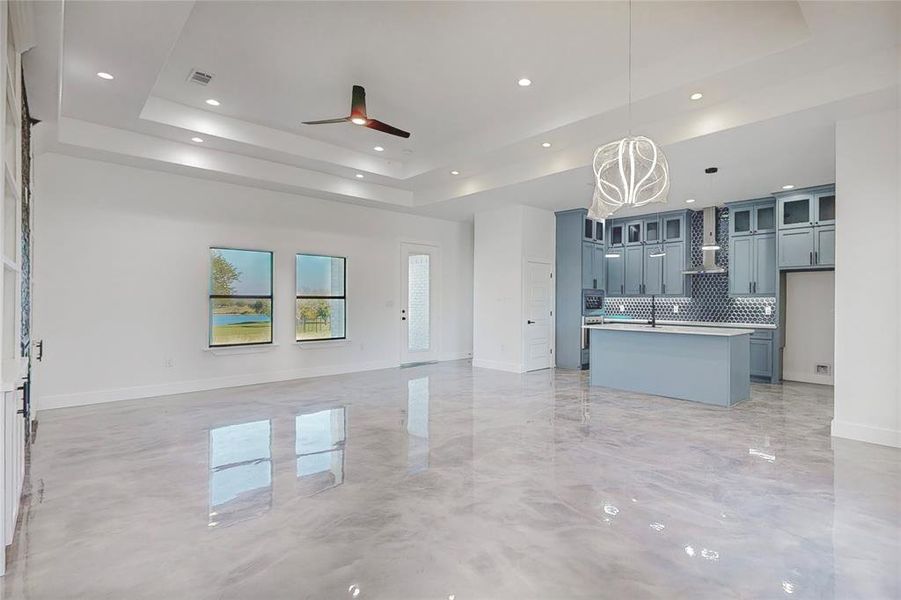 Unfurnished living room with ceiling fan with notable chandelier, sink, and a tray ceiling