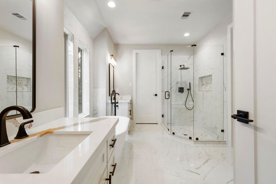 Another view to show off the freestanding tub, picture windows offering plenty of natural light, a sleek vanity with a mirror, and a spacious glass shower. The light tile flooring and neutral walls create an airy and elegant atmosphere. This en-suite features two closets