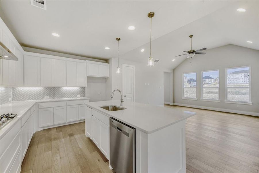 Kitchen featuring white cabinets, stainless steel appliances, light wood-style floors, and a kitchen island with sink