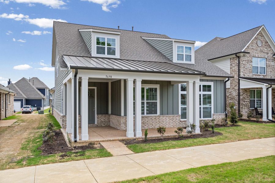 View of front of house with covered porch, a shingled roof, brick siding, and a standing seam roof