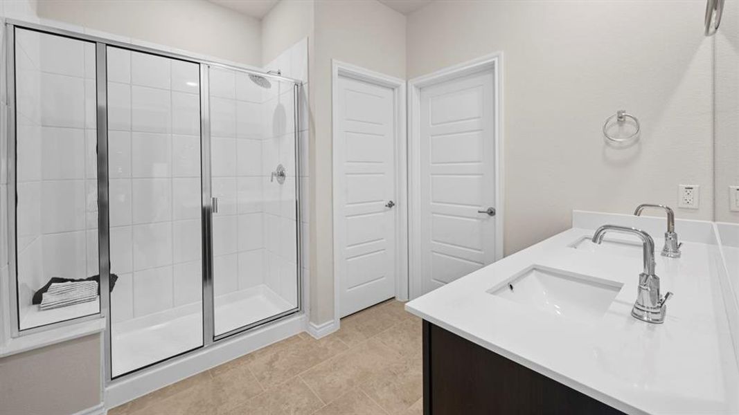 Full bath with double vanity, a stall shower, and light tile patterned floors