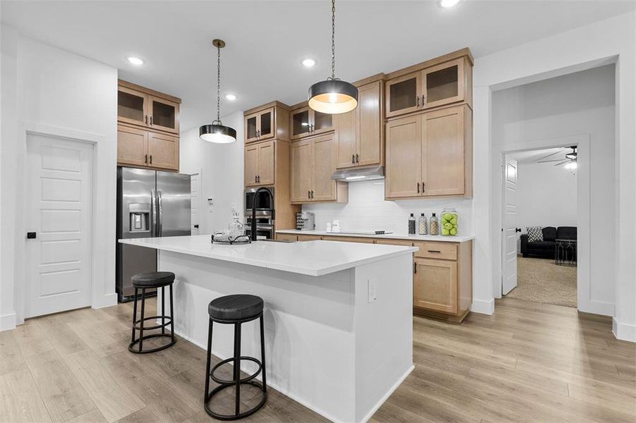 Kitchen with light hardwood / wood-style floors, appliances with stainless steel finishes, hanging light fixtures, and a center island with sink