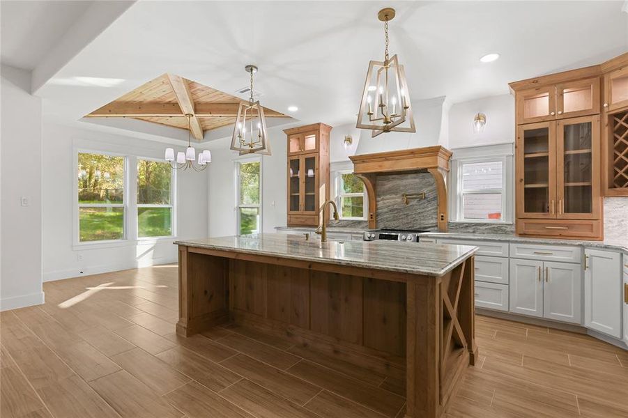 Kitchen featuring decorative backsplash, pendant lighting, light stone counters, wood finish floors, and an island with sink