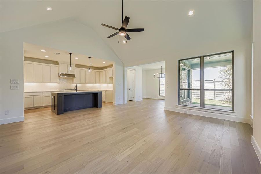 Unfurnished living room featuring high vaulted ceiling, ceiling fan, light wood finished floors, recessed lighting, and a chandelier Unfurnished living room featuring high vaulted ceiling, ceiling fan, light wood finished floors, recessed lighting, and a chandelier
