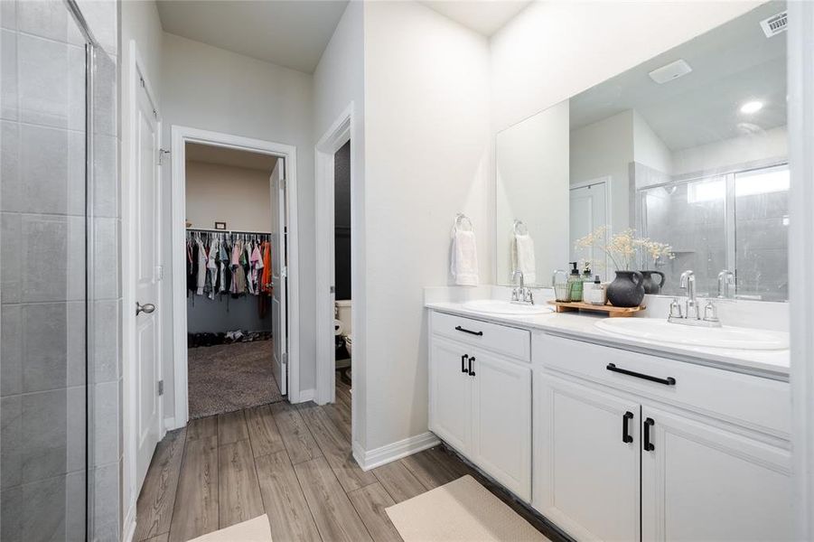 Bathroom featuring a shower stall, a spacious closet, double vanity, and light wood finished floors