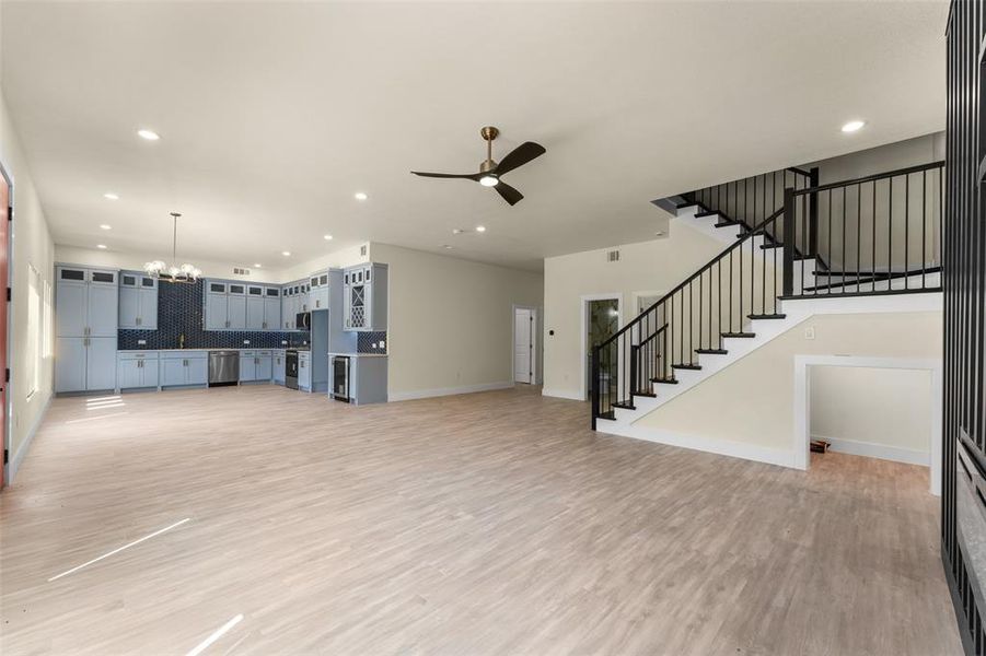 Unfurnished living room featuring a ceiling fan, light wood-style flooring, a chandelier, stairway, and recessed lighting